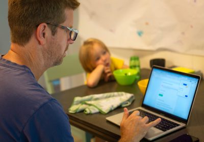 A dad sitting next to his kid at home while trying to work on the computer. Busy dads.