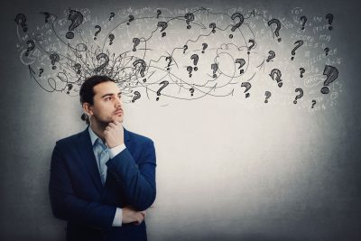 Thoughtful businessman keeps hand under chin, looking away pensive. Reflective business person planning and hard thinking for ideas. Mess calculations and question marks over head
