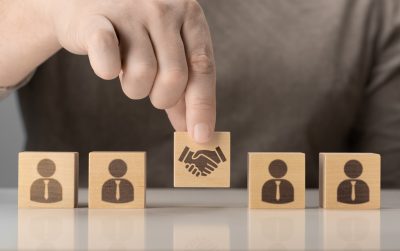 business contract. Hand putting hand shaking on wooden cube block in front of human icon for business deal and agreement concept. Business communication concept. Marketing. Shaking hands. Teamwork.