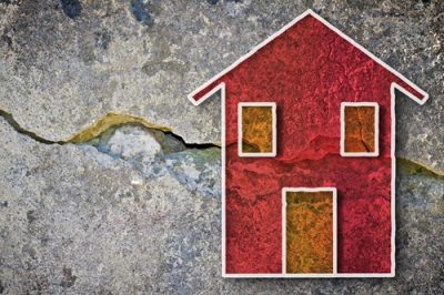 Deep crack in old brick wall with damaged plaster and colored house drawn on it - concept image with copy space